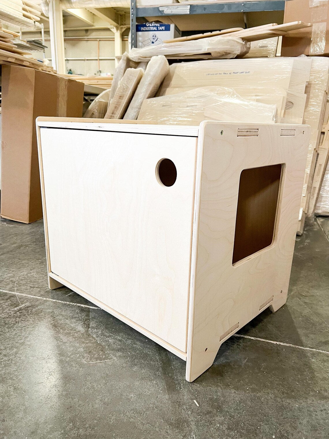 Wooden litter box cubby in a warehouse setting with cardboard boxes and wooden planks.