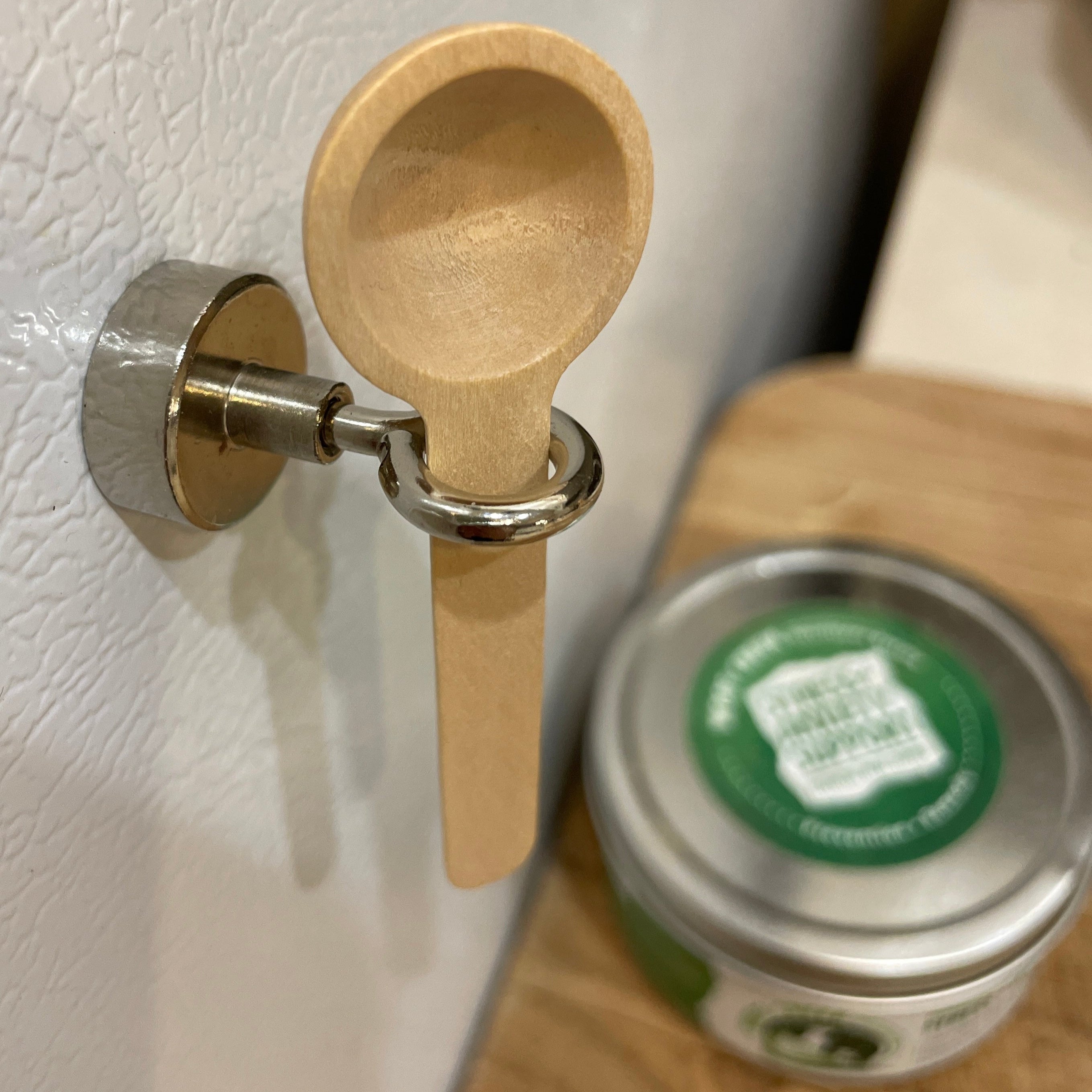 Wooden scoop attached to a refrigerator with a can of food in the foreground.