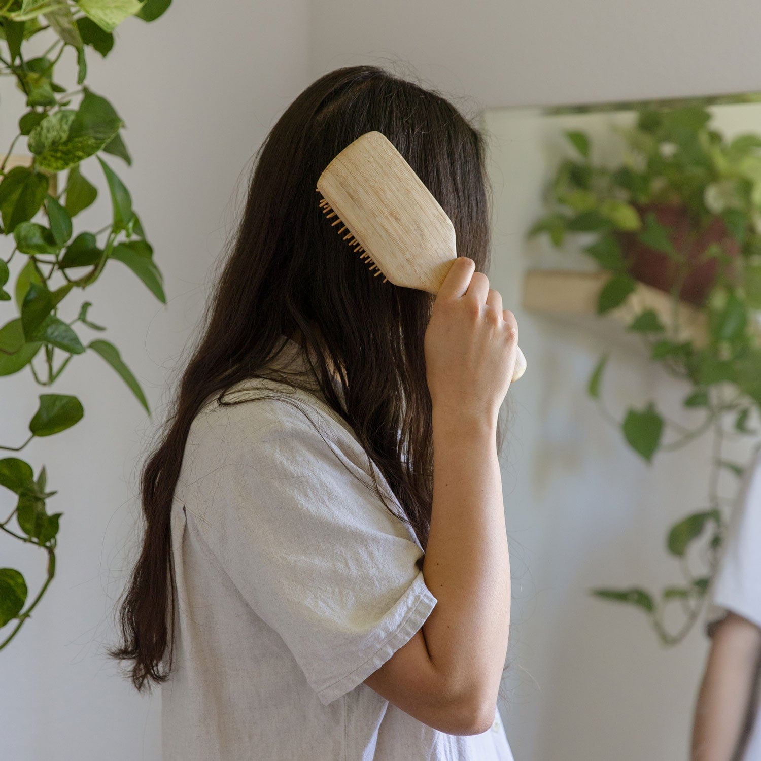 Person brushing their hair in front of a mirror with plants in the background
