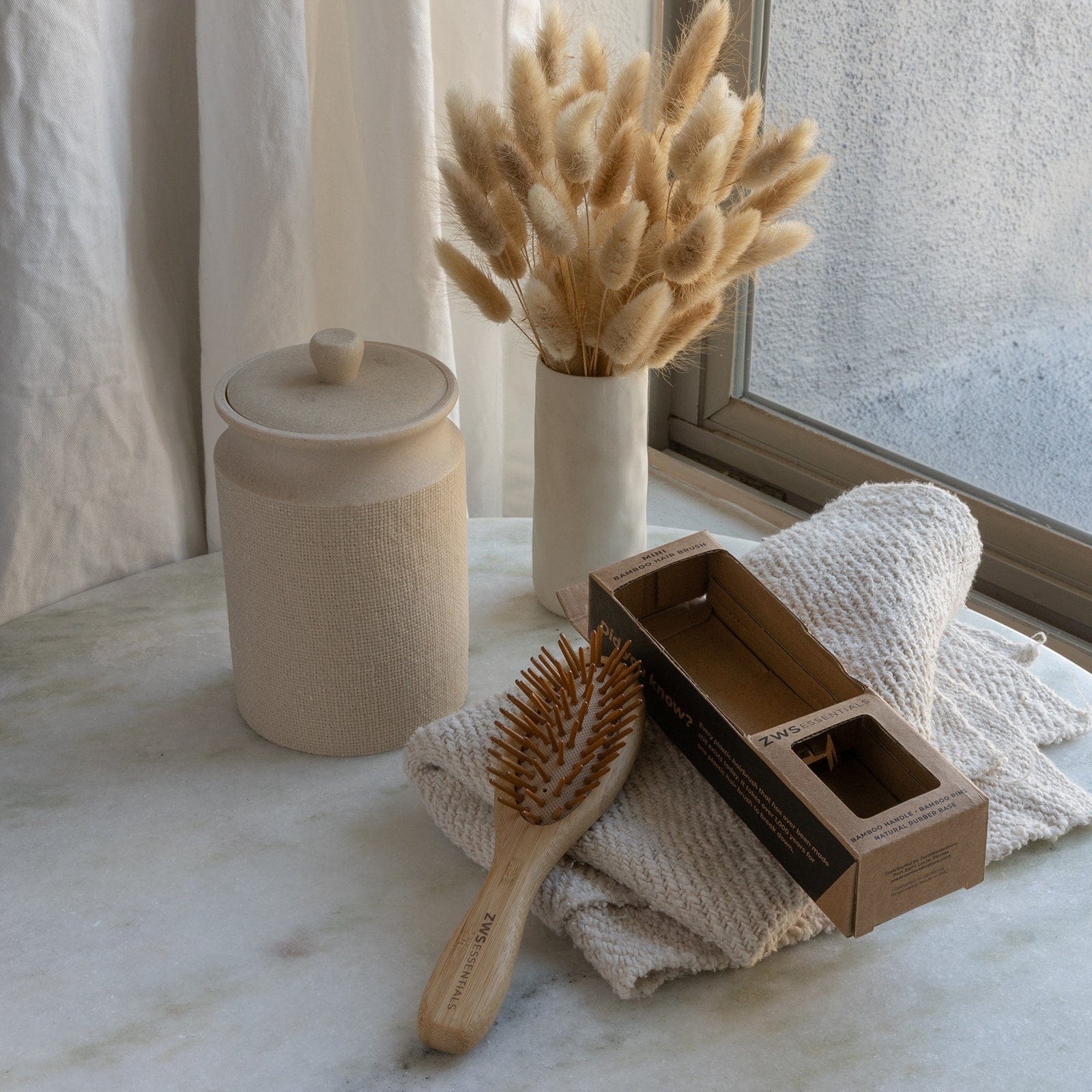 Hairbrush, box, towel, and vase with dried flowers on a marble surface.