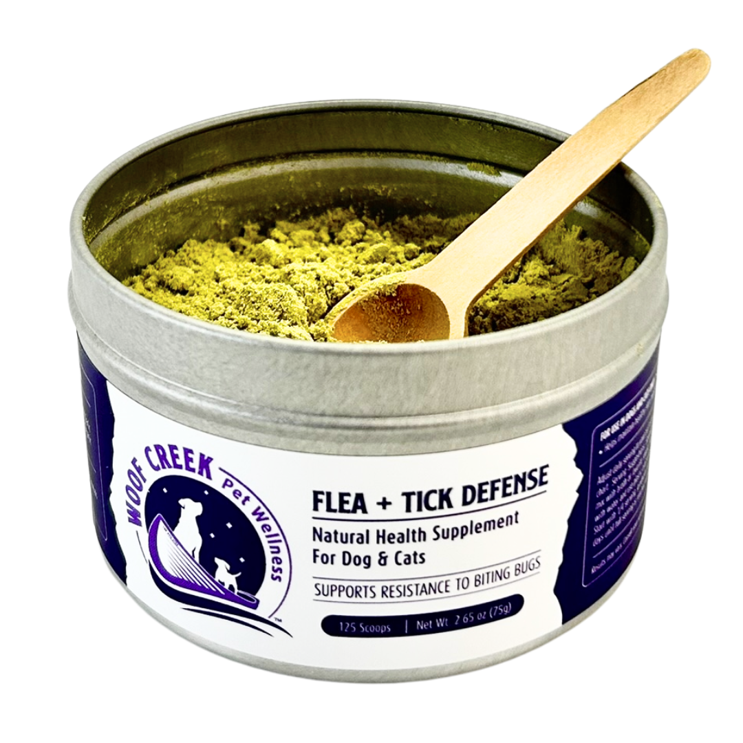 Tin of 'Flea + Tick Defense' natural health supplement for pets with a wooden spoon inside, on a white background.