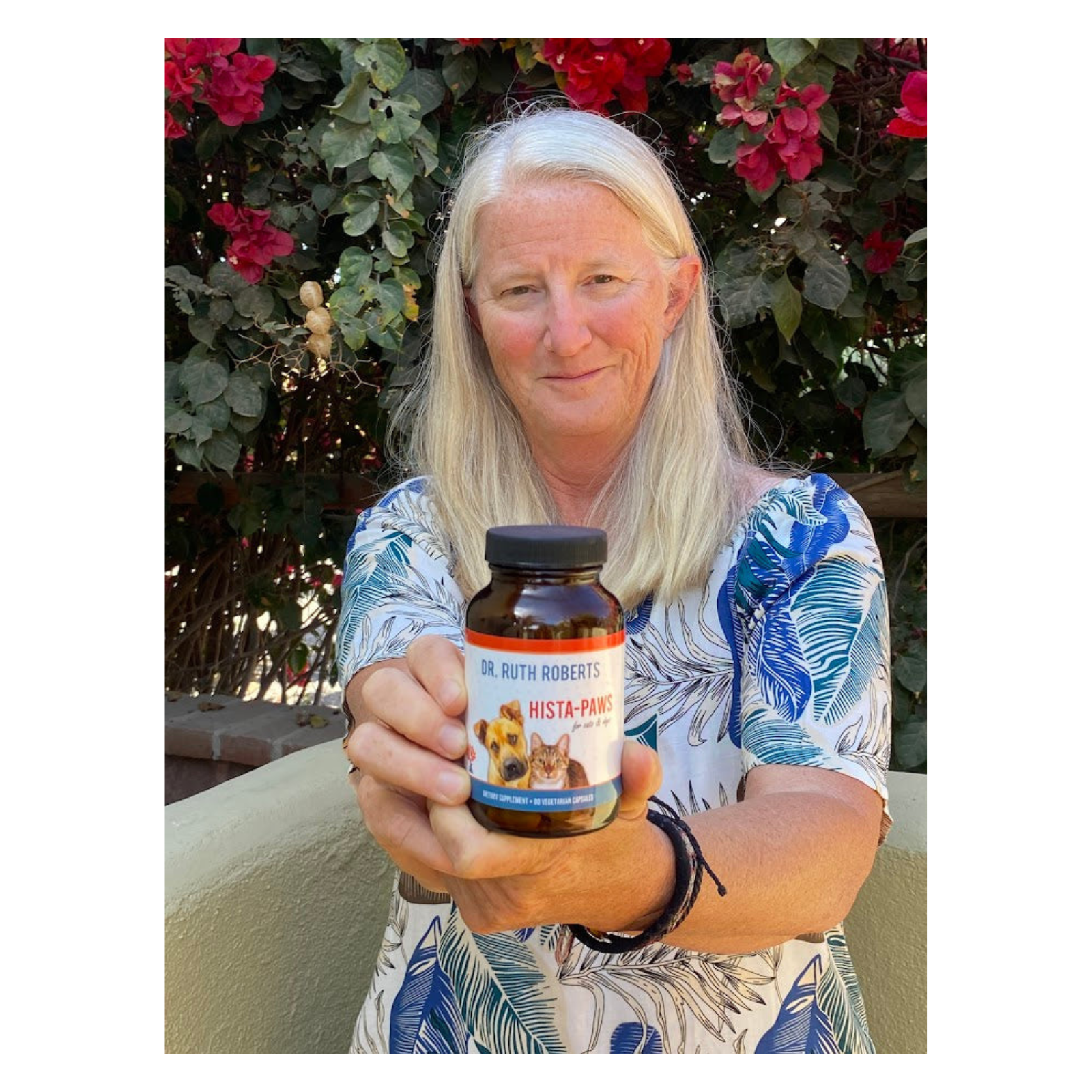 Dr. Ruth holding a bottle of 'Hista-Plus' supplement with flowers in the background