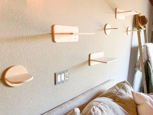 Wooden cat wall shelves on a textured wall above a bed with pillows.