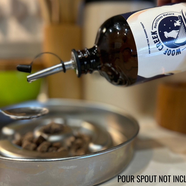 Bottle of pet supplement being poured into a metal bowl with a spoon, on a kitchen counter.