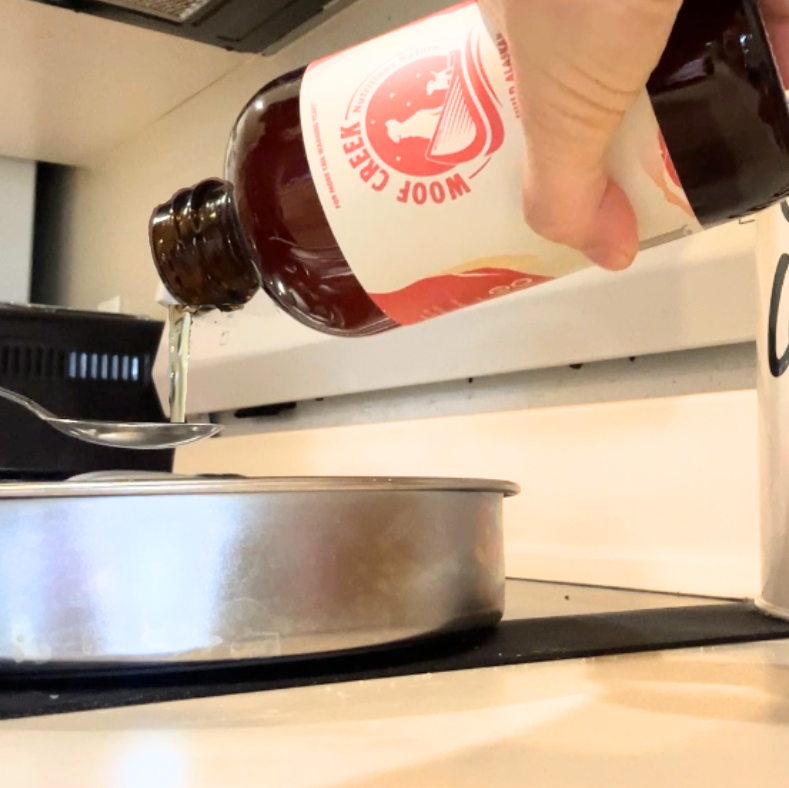 Hand pouring a bottle of Woof Creek fish oil into dog food.