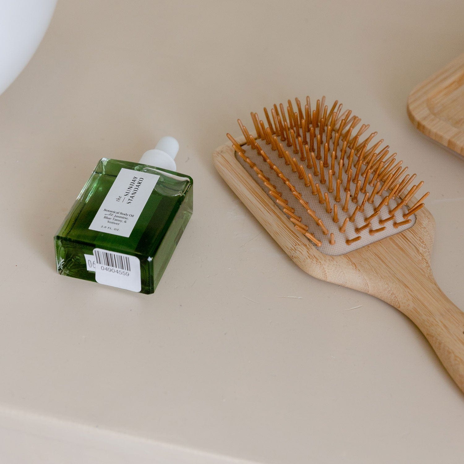 Green hair product bottle and wooden hairbrush on a beige surface