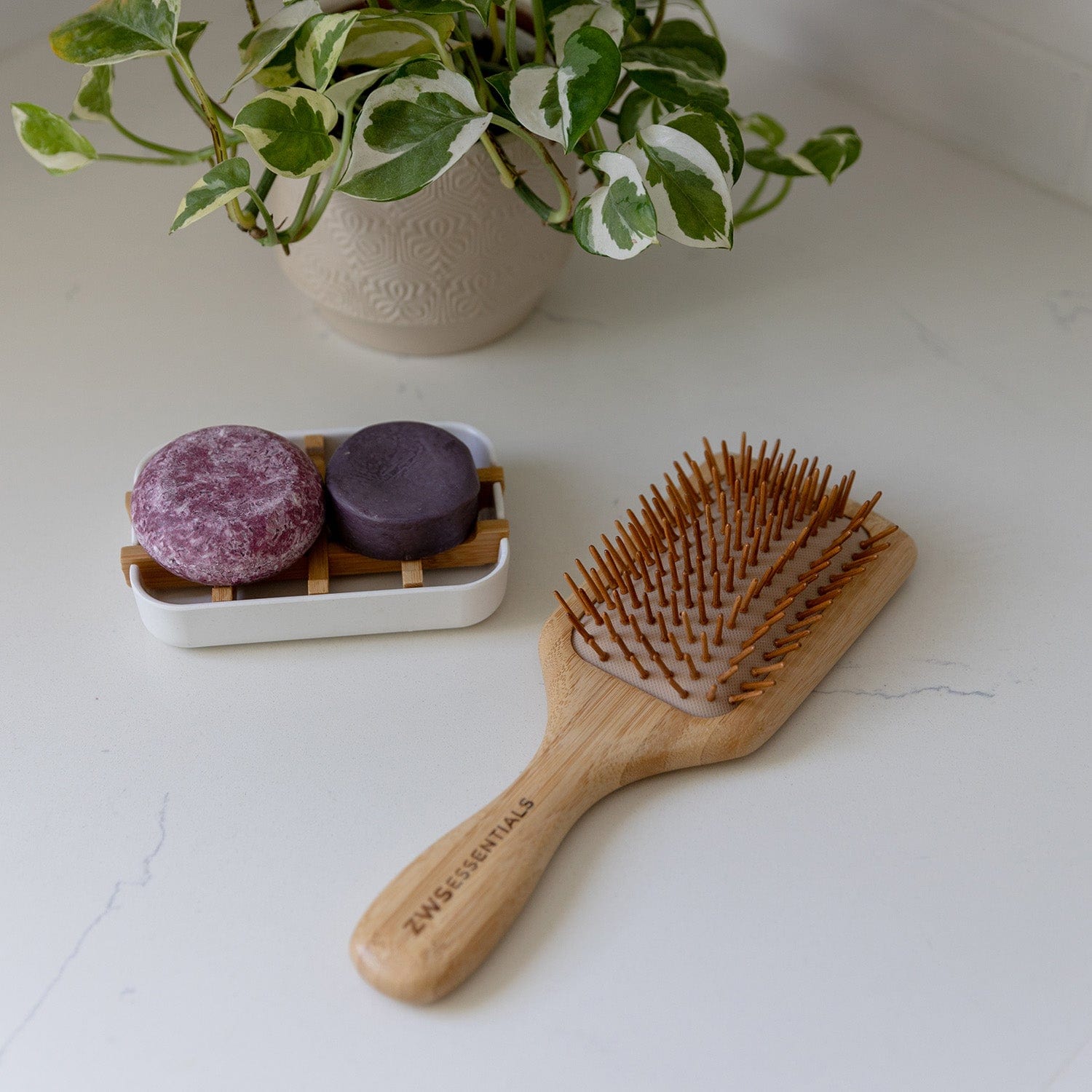 Wooden hairbrush on a white surface with two purple bath bombs and a plant in the background.