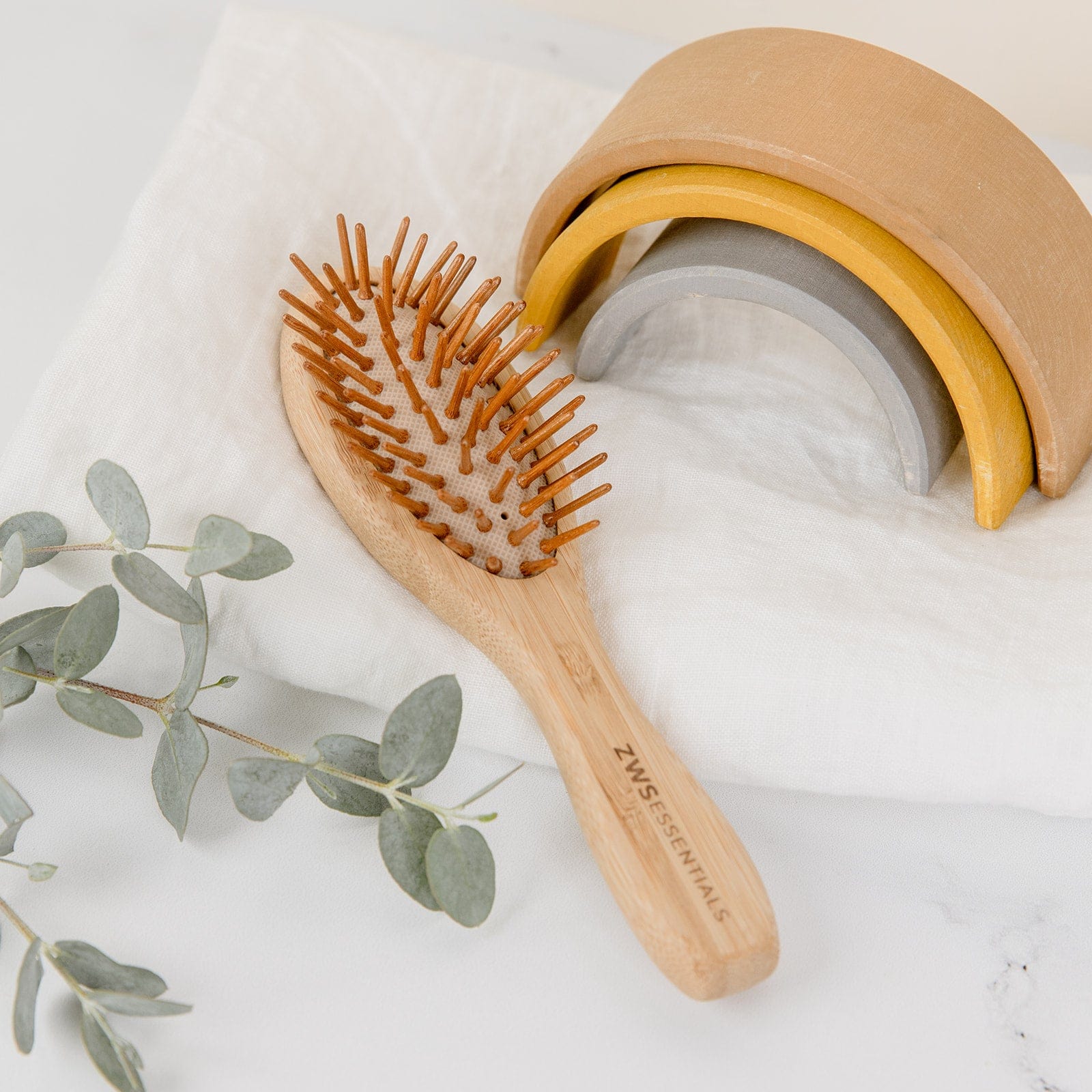 Wooden hairbrush with a beige container and eucalyptus leaves on a light background